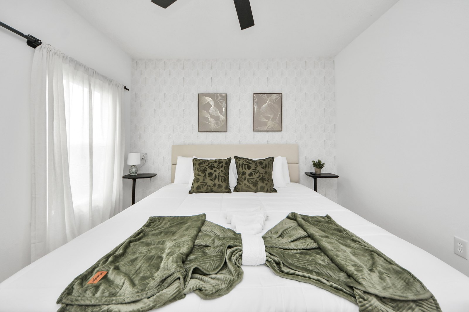 Spacious primary bedroom with a king bed, upholstered headboard, layered linens, framed art, and bright windows