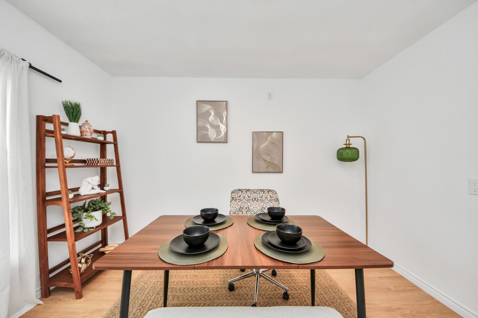 Walnut dining table set for four with black stoneware, woven placemats, and a green glass floor lamp