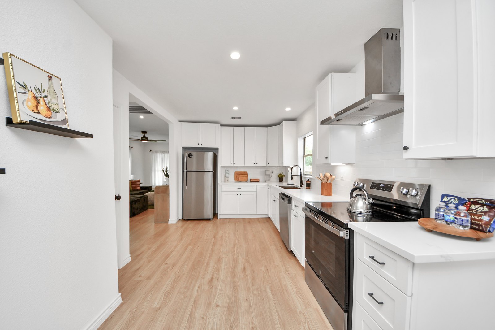 Renovated white kitchen with quartz counters, stainless refrigerator and range, dishwasher, and gallery-wall art